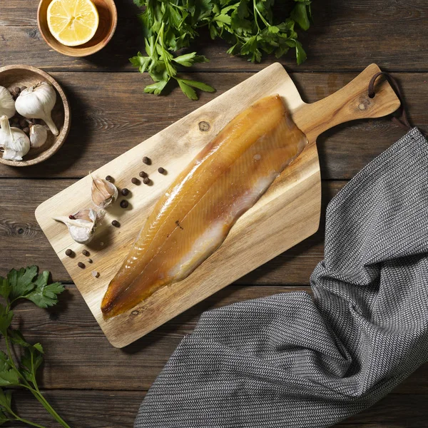 Cold smoked muksun fish on a wooden Board on a brown wooden table. Whole fillet of fish whitefish or muksun closeup. Top view with space for text.