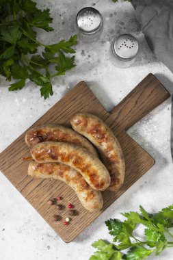 Açık gri bir mutfak masasında ahşap bir tahtanın üzerinde ızgara sosisler. Üst Görünüm