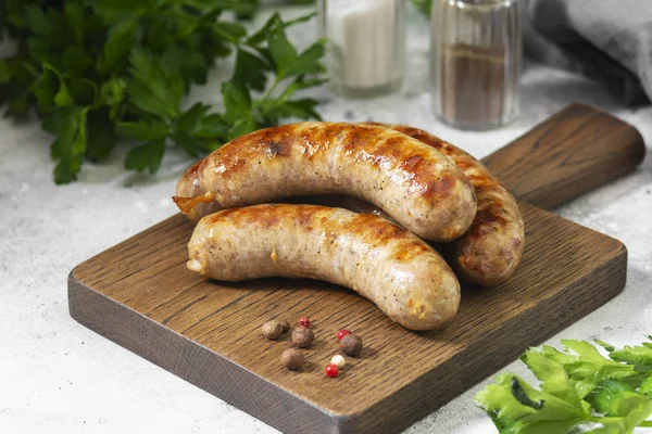 Açık gri bir mutfak masasında ahşap bir tahtanın üzerinde ızgara sosisler.