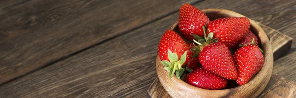 Strawberries in a wooden bowl on a wooden table. Banner