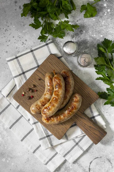 Açık gri bir mutfak masasında ahşap bir tahtanın üzerinde ızgara sosisler. Üst Görünüm