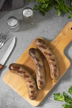 Açık gri bir mutfak masasında ahşap bir tahtanın üzerinde ızgara sosisler. Üst Görünüm