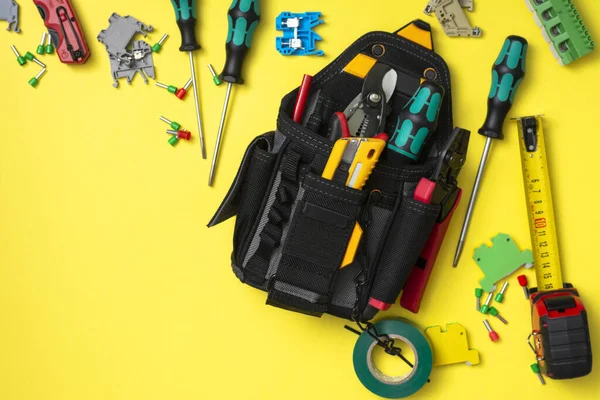 Construction tools of the installer in a black bag on a yellow background. Electrician tools and project. Top view with a copy of the text space. Horizontal orientation