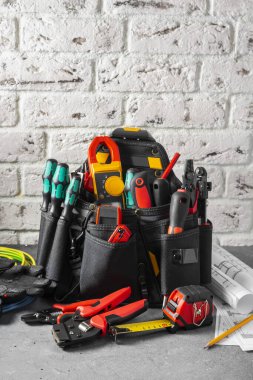 Elektrikçi aletleri siyah bir çantada gri bir masada beyaz bir duvara karşı. Kurucu ya da elektrikçinin inşaat aletleri. Metin için boşluk