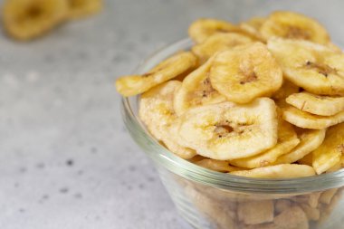 Dried bananas in a glass bowl on a gray kitchen table. Banana chips. Vegetarian snack for proper nutrition