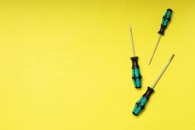 Sarı arka planda üç tornavida. Kurucu ya da elektrikçinin inşaat aletleri. Metin alanının bir kopyasıyla en üstteki görünüm.