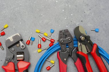 Elektrik kablolarını sıkıştırmak için farklı boylarda ve renklerde aletler ve uçlar. Gri beton arka planda kripto aletleri, kablo uçları ve elektrik kablosu