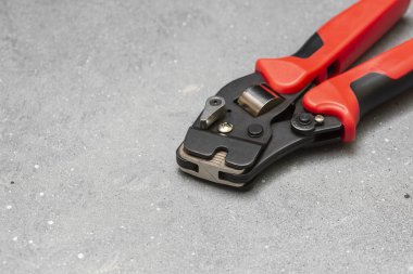 Elektrik kablolarını sıkıştırmak için bir araç. Gri beton arka planda bir elektrikçi veya inşaatçı için kripto aracı