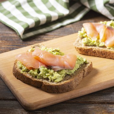 Kahverengi ahşap bir masanın üzerinde, ahşap bir tahtanın üzerinde avokado ve somon balığıyla Avokado ve kırmızı balıklı kızarmış ekmek. Konsept kullanışlı ve lezzetli Kahvaltı