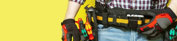 Electrician or professional Builder in the installer's belt with tools on a yellow background. Electrician's tools in black bags on the worker 's belt. Banner with space for text