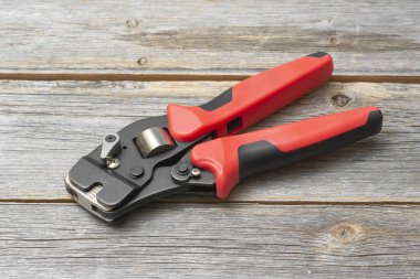 Elektrik kablolarını sıkıştırmak için bir araç. Gri ahşap arka planda elektrikçi veya inşaatçı için kripto aracı