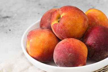 Açık gri bir masada beyaz bir tabakta şeftali. Kapatın. Mevsimlik meyveler