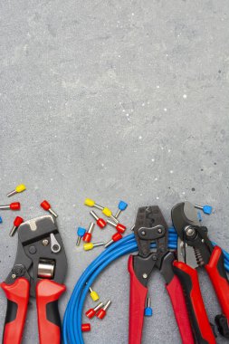 Elektrik kablolarını sıkıştırmak için bir araç. Gri beton arka planda bir elektrikçi veya inşaatçı için kripto aracı