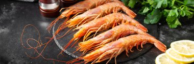 Siyah mutfak masasının üstünde siyah bir tabakta büyük Langoustines. Sağlıklı beslenme için deniz ürünleri. Pankart