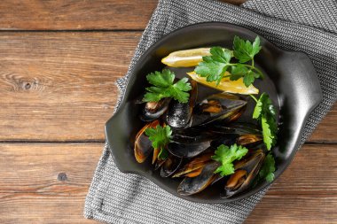 Kahverengi ahşap bir masada siyah seramik tabakta midye pişirdim.