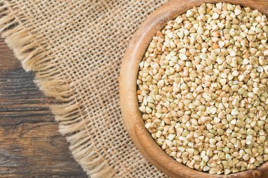 Kahverengi ahşap bir masada tahta bir kasede çiğ yeşil karabuğday. Metin için boşluk olan üst görünüm