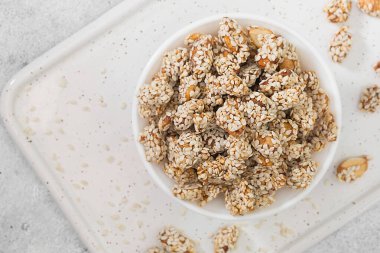 Bal şurubunda kavrulmuş fıstık ve açık gri mutfak masasındaki beyaz kasede susam tohumları. Metin için boşluk olan üst görünüm. Kapat.
