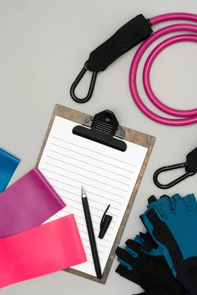 Expanders for fitness and elastic bands for sports, as well as an open notebook with a pen for drawing up a training schedule on a gray background. The concept of drawing up a sports training plan — Stock Image Expanders Fitness Elastic Bands Sports Well Open Notebook Pen Drawing Stock Picture