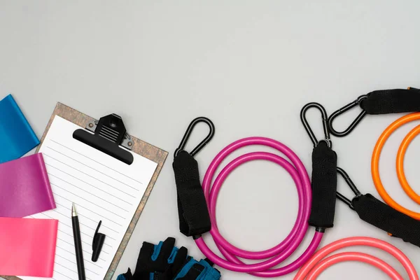 Expanders for fitness and elastic bands for sports, as well as an open notebook with a pen for drawing up a training schedule on a gray background. The concept of drawing up a sports training plan — Stock Image Expanders Fitness Elastic Bands Sports Well Open Notebook Pen Drawing Stock Photo