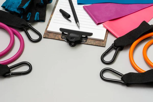 Expanders for fitness and elastic bands for sports, as well as an open notebook with a pen for drawing up a training schedule on a gray background. The concept of drawing up a sports training plan — Stock Image Expanders Fitness Elastic Bands Sports Well Open Notebook Pen Drawing Stock Photo