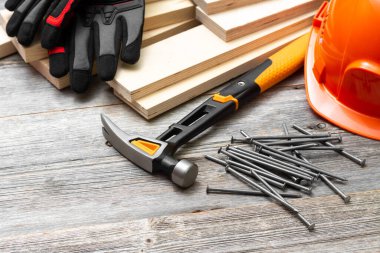 Marangozluk aletleri çekiç, çivi, tahta parmaklıklar, miğfer ve eldivenler gri tahta bir masada.