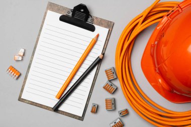 Elektrikçi veya Mimar 'ın turuncu miğferi, gri arka planda tel, araba ve not defteri. Yukarıdan görünüşü