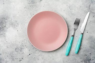 Gri mutfak masasında boş bir pembe tabak ve çatal bıçak takımı.