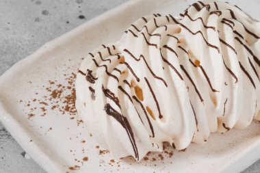 Açık gri bir masada beyaz bir tabağa çikolatalı krema döküldü.