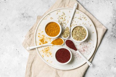 Beyaz bardaklarda baharatlar ve açık gri bir masada kaşıklar. Fennel, sumac, beyaz kaselerde köri. Metin için yeri olan baharatlar. Yukarıdan manzara. Pankart.