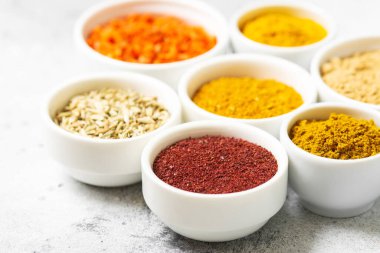 Açık gri bir masada beyaz kâselerde baharatlar ve baharatlar. Beyaz kaselerde zerdeçal, zencefil, köri, rezene ve sumak. Baharatlar metin için boşluk ile kapanır