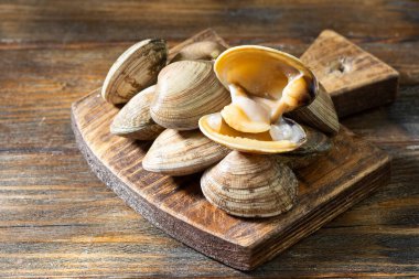 Kahverengi ahşap bir masada tahta bir tahta üzerinde çiğ istiridye. Deniz kabuğu