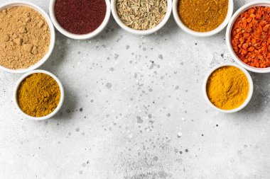Açık gri bir masada beyaz kâselerde baharatlar ve baharatlar. Beyaz kaselerde zerdeçal, zencefil, köri, rezene ve sumak. Metin için boşluk olan üst görünüm