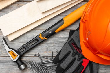 Marangozluk aletleri çekiç, çivi, tahta parmaklıklar, miğfer ve eldivenler gri tahta bir masada.