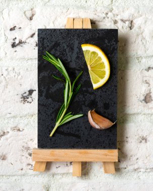 Bir tutam biberiye, bir dilim limon ve beyaz tuğlalı arka planda tahta üzerinde bir diş sarımsak. Resim, kartpostal veya takvim kavramı