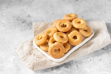 Açık gri arka planda beyaz bir tabağa şeker serpiştirilmiş puf böreği. Kurabiyelere şeker serpilmiş. Tatlı hamur işleri