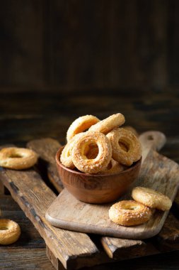 Kahverengi ahşap arka planda ahşap bir kaseye şeker serpiştirilmiş poğaça. Kurabiyelere yakın plan şeker serperim. Tatlı hamur işleri