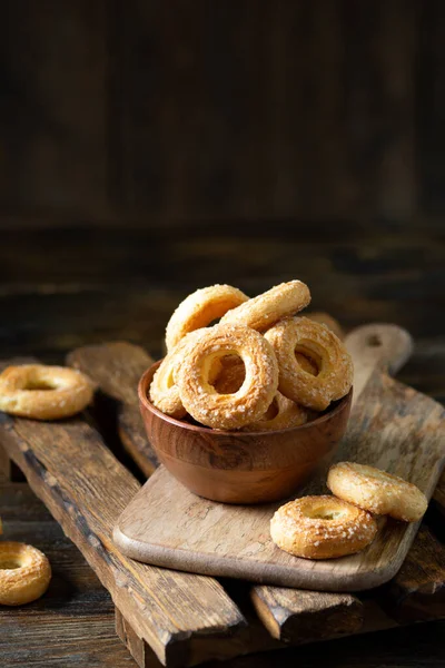 Kahverengi ahşap arka planda ahşap bir kaseye şeker serpiştirilmiş poğaça. Kurabiyelere yakın plan şeker serperim. Tatlı hamur işleri
