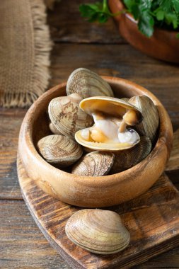 Kahverengi ahşap bir masada tahta bir kasede çiğ istiridye. Deniz kabuğu