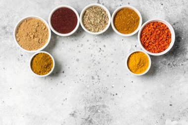 Açık gri bir masada beyaz kâselerde baharatlar ve baharatlar. Beyaz kaselerde zerdeçal, zencefil, köri, rezene ve sumak. Metin için boşluk olan üst görünüm