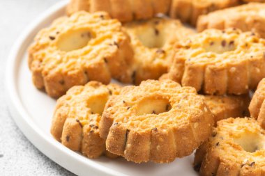 Açık gri mutfak masasında büyük beyaz bir seramik tabakta çörekler. Tabakta bir sürü kurabiye var. Ev yapımı lezzetli hamur işleri. Kapalı tabakta kurabiyeler.