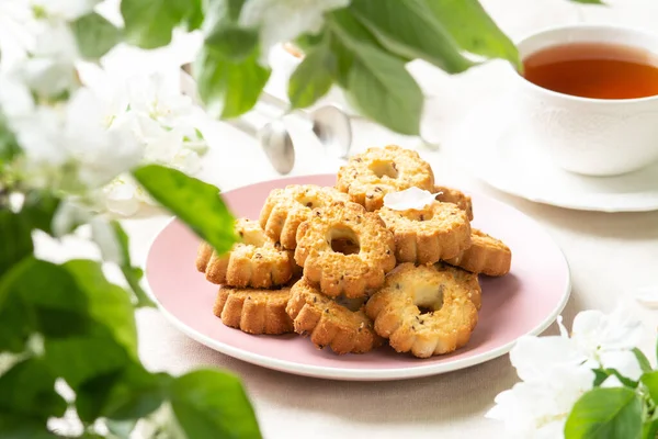 Shortbread in a pink ceramic plate on a light table. A plate of cookies on the table among the flowering trees. The plate is full of cookies. Rustic homemade cakes. Tea party with pastries