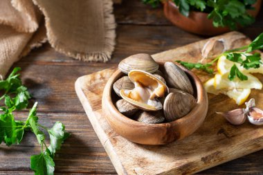 Kahverengi ahşap bir masada tahta bir kasede çiğ istiridye. Deniz kabuğu