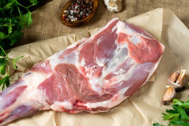 Kahverengi ahşap bir masadaki parşömen üzerinde çiğ koyun bacağı. Yakın plan koyun eti. Masada taze bir kuzu eti var. Üst görünüm