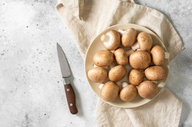Açık gri mutfak masasında bej bir tabakta çiğ mantar. Mutfak arka planında tabakta mantarlar. Metin için boşluk olan üst görünüm