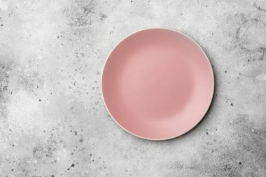 Açık gri bir masada pembe bir tabak. Masanın üzerinde boş pembe bir tabak. Yukarıdan görünüşü