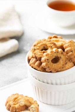 Işık masasında beyaz bir seramik kasede çörekler. Gri mutfak masasında bir tabak kurabiye ve bir fincan çay. Bir tabak dolusu kurabiye. Ev yapımı keklerle çay partisi.