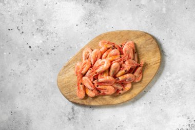 Açık gri mutfak masasında tahta tahtada karidesler. Servis kurulunda bir sürü karides var. Metin için boşluk olan üst görünüm