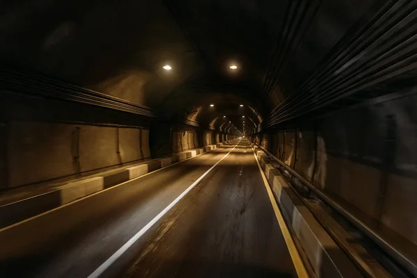 Road tunnel in mountain illuminated by lamps