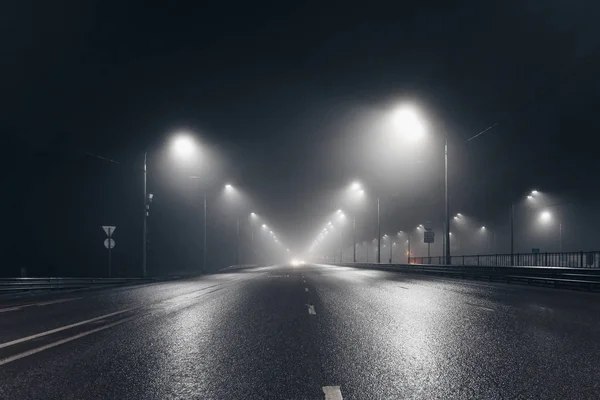 Foggy misty night road and overhead pedestrian bridge illuminated by street lights — 图库照片