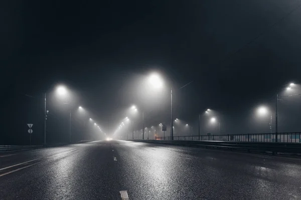 Foggy misty night road and overhead pedestrian bridge illuminated by street lights — 图库照片